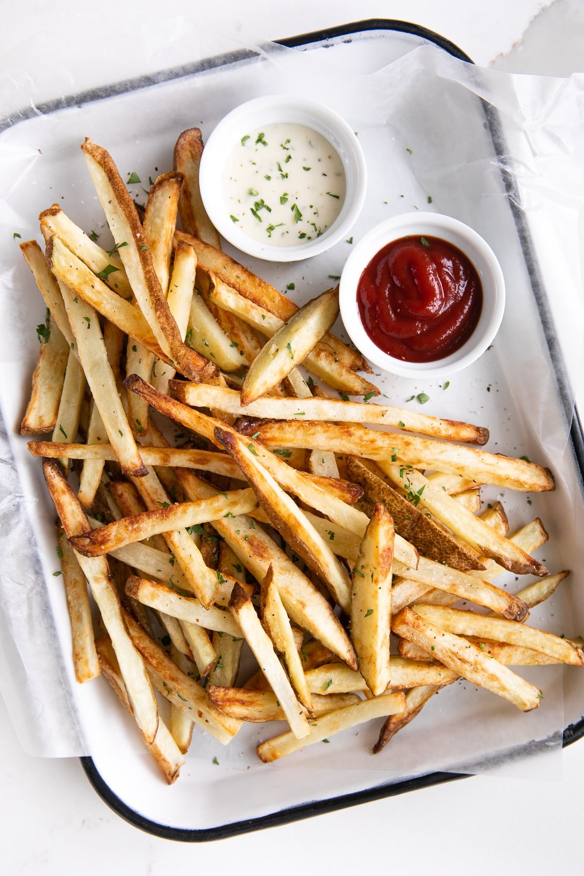 Overhead view of a tray of golden brown air fryer French fries with ketchup and ranch on the side.