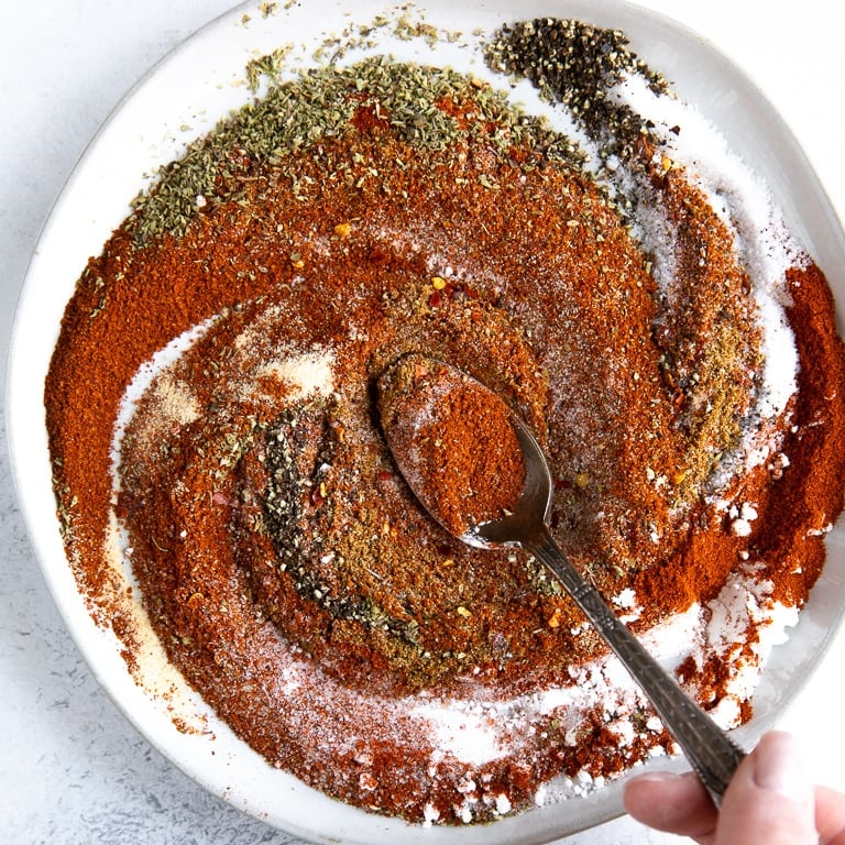 Shallow white bowl filled with various different seasonings mixing together.