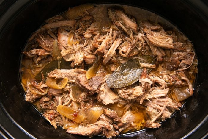 Fully cooked carnitas pork butt in a large slow cooker that's ready to be shredded.