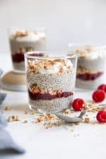 Small glass jars filled with chia seed pudding layered with granola and raspberry jam.