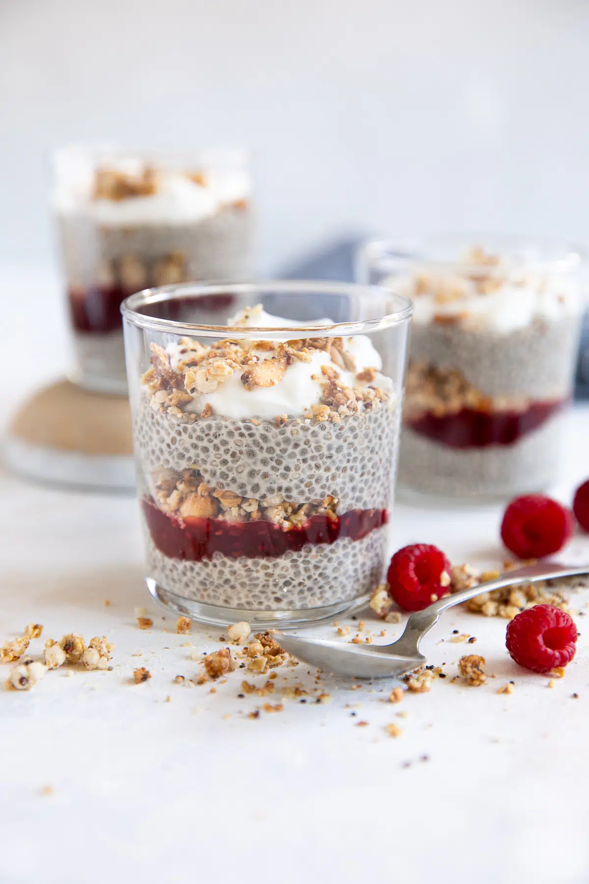 Small glass jars filled with chia seed pudding layered with granola and raspberry jam.