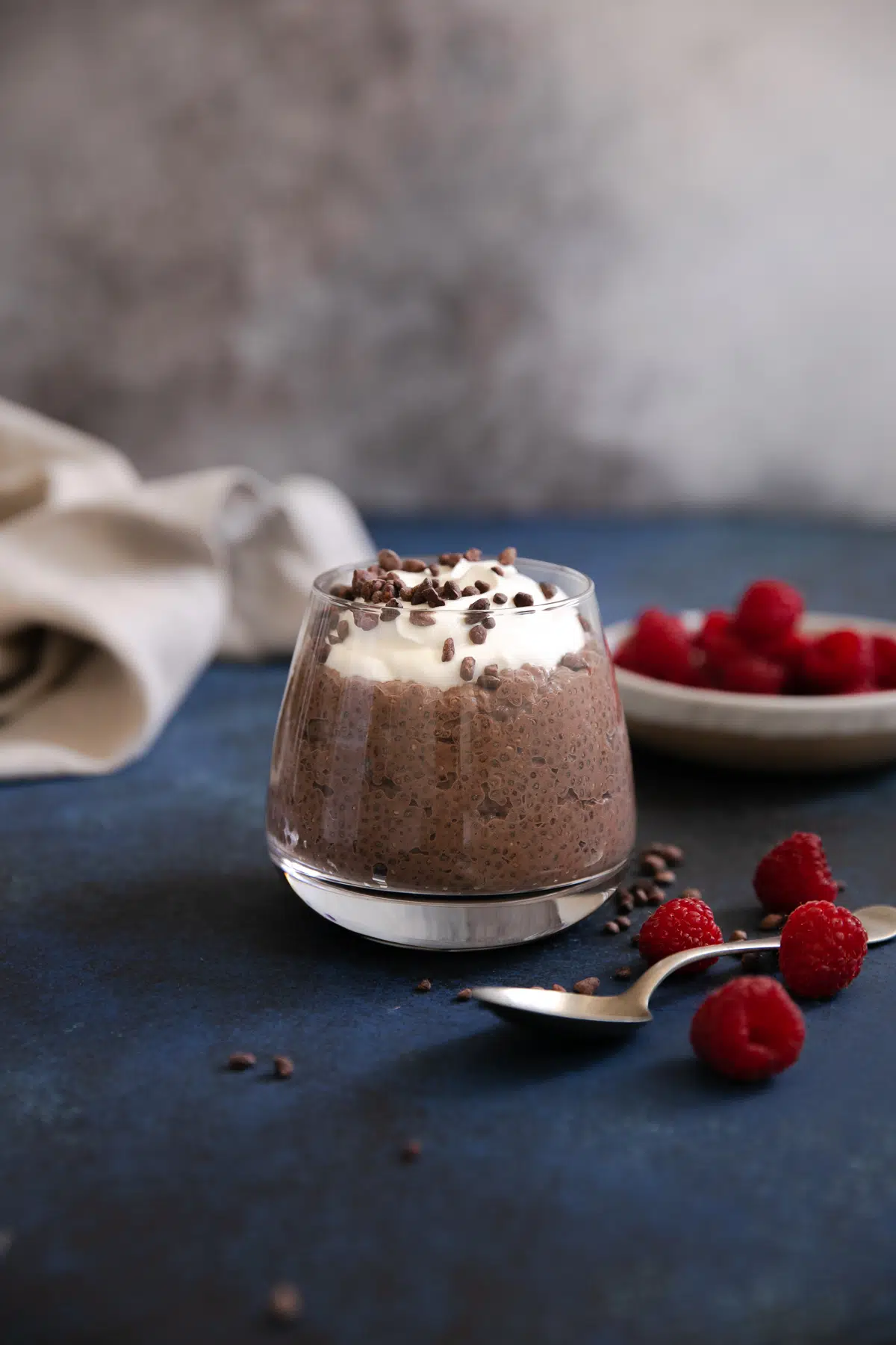 Glass jar filled with creamy chocolate chia pudding and topped with vanilla Greek yogurt, cocoa nibs, and served with a side of fresh raspberries.