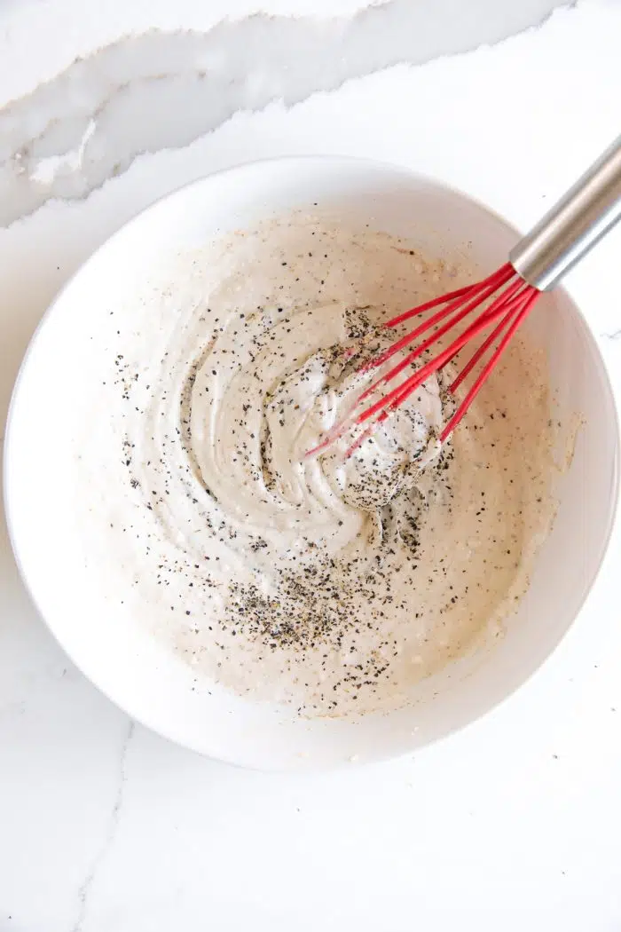 White bowl filled with creamy mayo dressing seasoned with black pepper.
