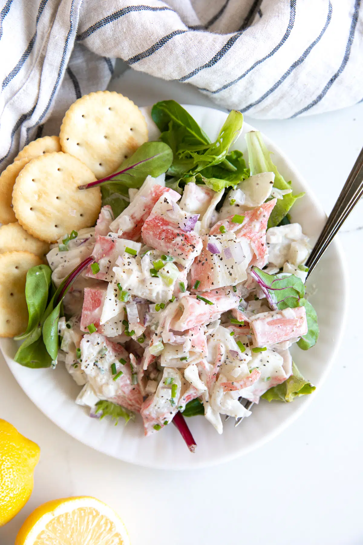 Crab salad served over mixed greens and served with buttery crackers on a white plate.