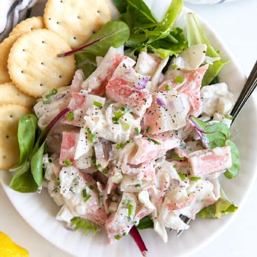 Crab salad served over mixed greens and served with buttery crackers on a white plate.