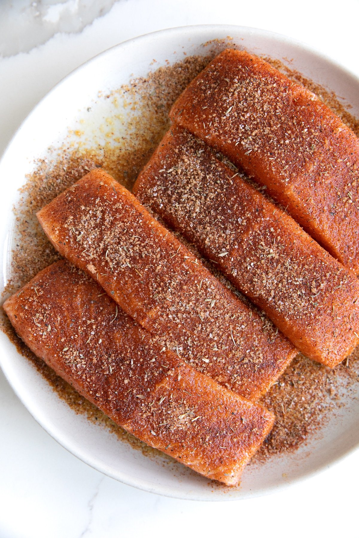 Four seasoned salmon fillets on a white plate.