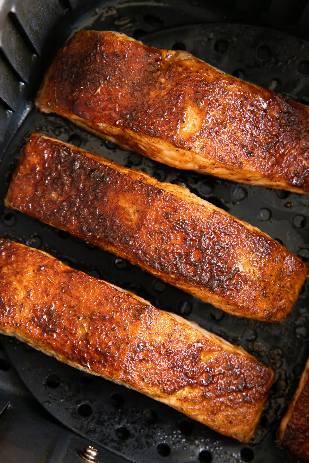 Three cooked salmon fillets in an air fryer basket after cooking.