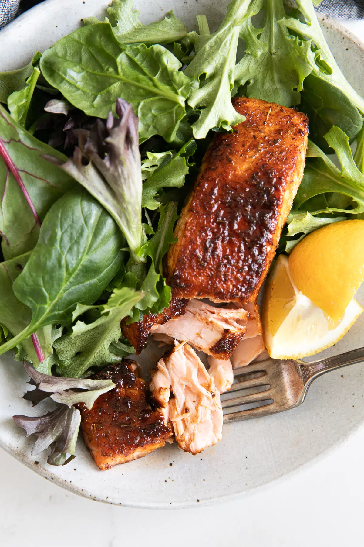 Serving plate with one salmon fillet and fresh greens.