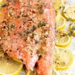 Baked salmon fillet on a bed of thinly sliced lemons and covered in a lemon, butter, garlic, and honey sauce. The top of the salmon is garnished with fresh thyme and red chili flakes.