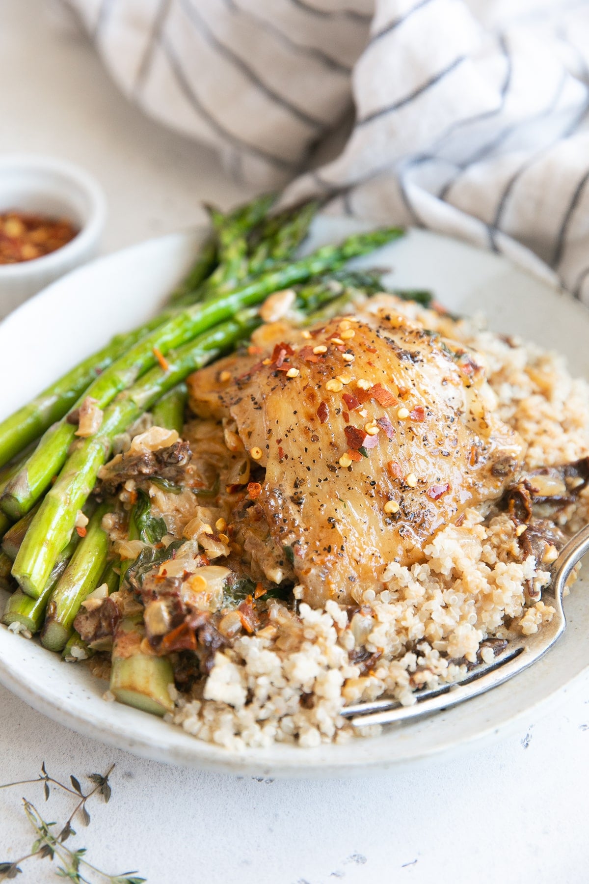 Plate filled with asparagus and quinoa topped with creamy Tuscan chicken.