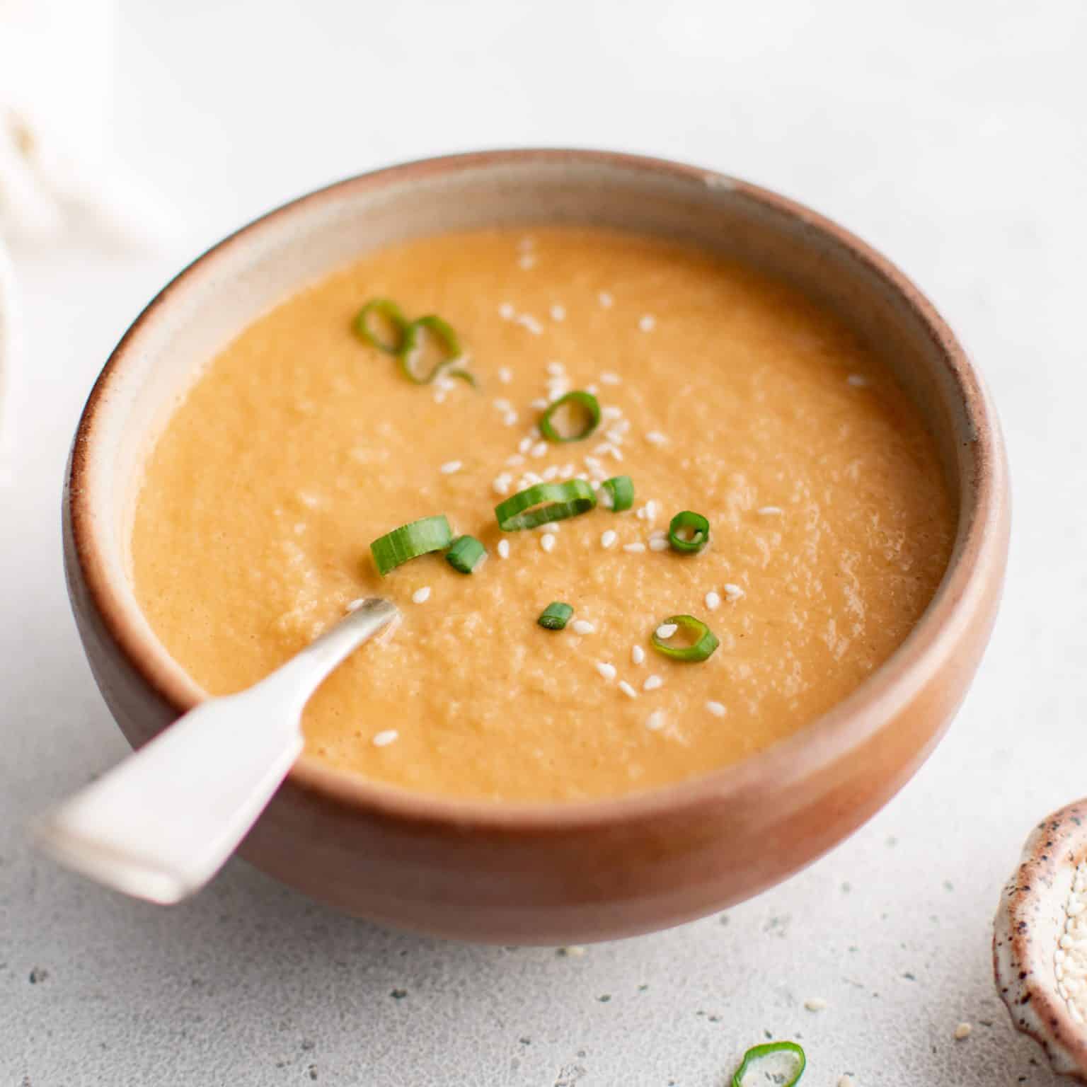 Creamy ginger dressing in a rustic bowl, garnished with sliced green onions and sesame seeds.