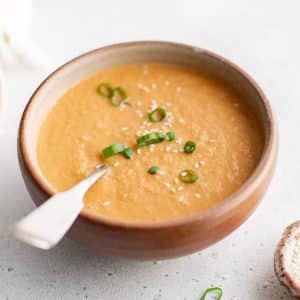 Creamy ginger dressing in a rustic bowl, garnished with sliced green onions and sesame seeds.