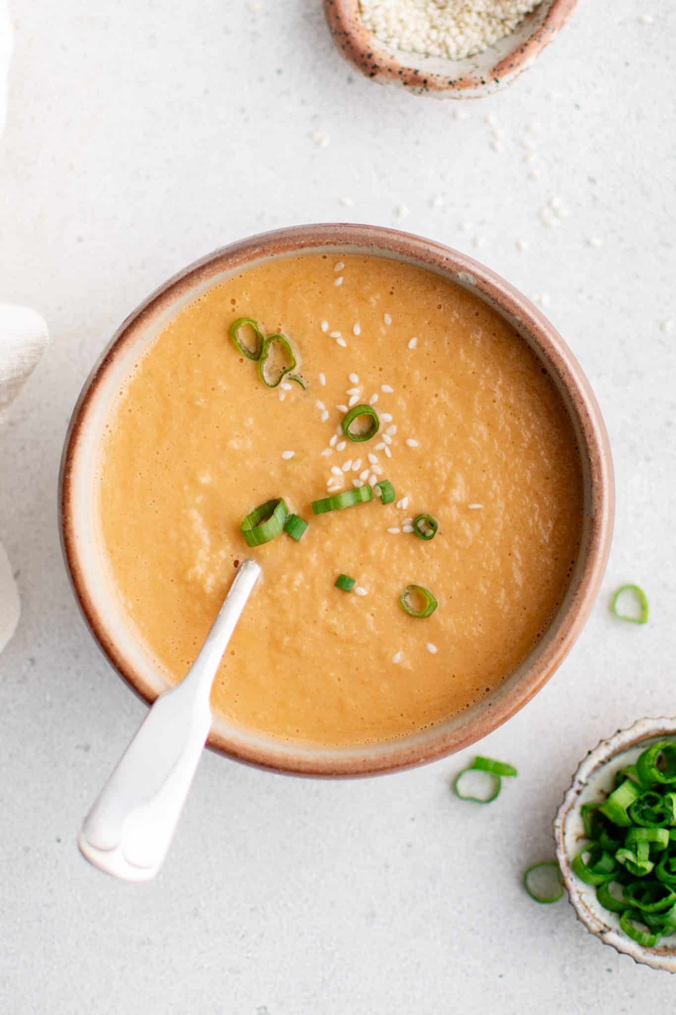 Overhead of ginger dressing in a bowl with spoon, garnished with green onions and sesame seeds.