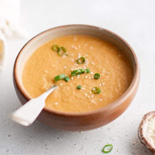 Creamy ginger dressing in a rustic bowl, garnished with sliced green onions and sesame seeds.