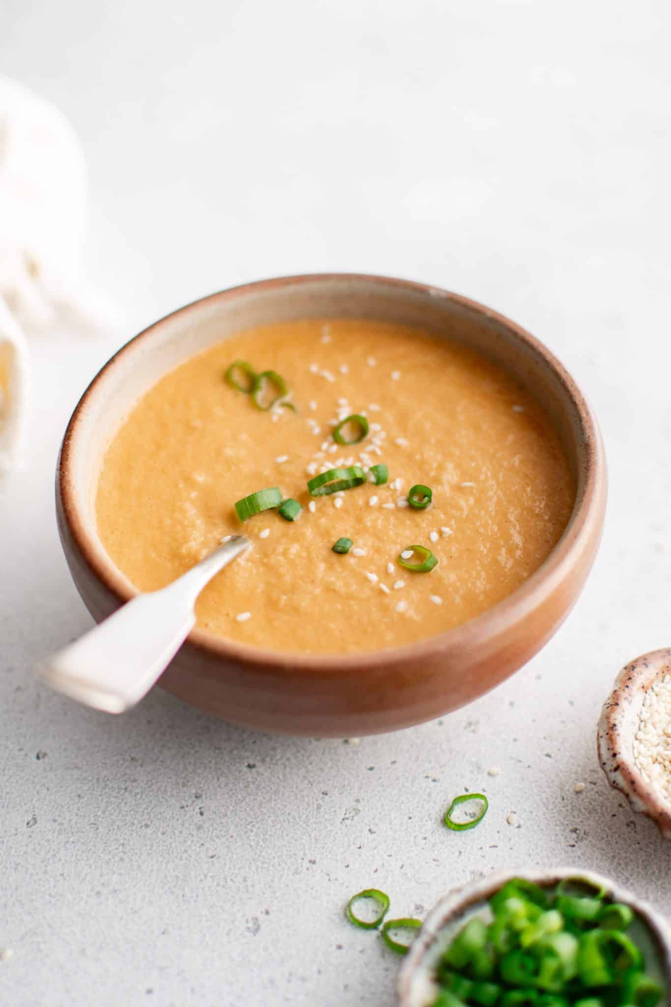Creamy ginger dressing in a rustic bowl, garnished with sliced green onions and sesame seeds.