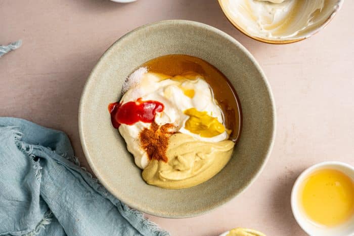 All the key ingredients—mayonnaise, Dijon mustard, yellow mustard, honey, white vinegar, hot sauce, cayenne, and salt—are added to a small mixing bowl in preparation for whisking.