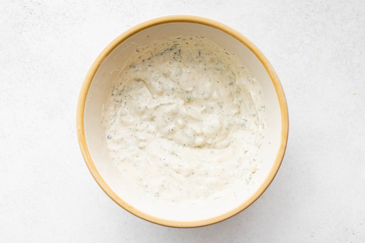 Overhead view of fully mixed tartar sauce in a beige bowl, showcasing a creamy texture with visible flecks of herbs and pickles.