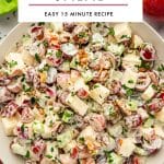 Vertical Pinterest graphic showing a light beige bowl filled with creamy Waldorf salad on a pale background, made with chopped red-skinned apples, halved red grapes, celery, and walnuts, garnished with chopped green parsley. Bright green lettuce leaves appear in the upper left corner, and a whole red apple is visible in the upper right corner. A large light gray text box overlays the upper center of the image with black text reading โWALDORF SALADโ and smaller black text below reading โEASY 15 MINUTE RECIPE,โ separated by a muted pink line. Small black text at the bottom reads โthe forked spoon.โ