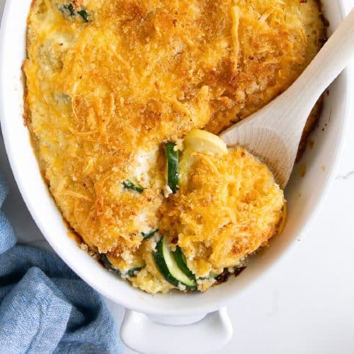 Creamy baked zucchini casserole in a white casserole dish and filled with rows of sliced zucchini and yellow squash and topped with a golden crust of panko breadcrumbs, and shredded cheese.