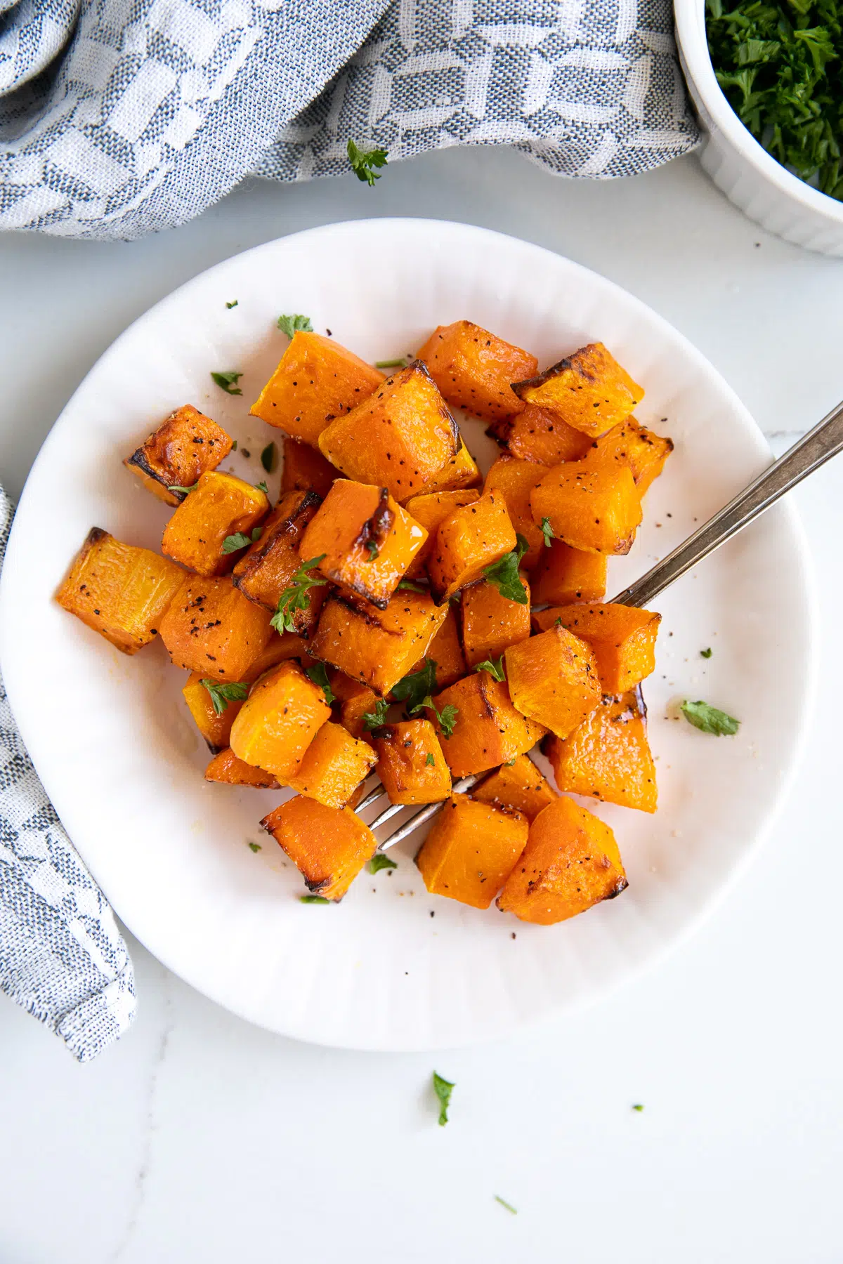 White plate filled with tender cubes of butternut squash cooked in the air fryer and garnished with chopped parsley.