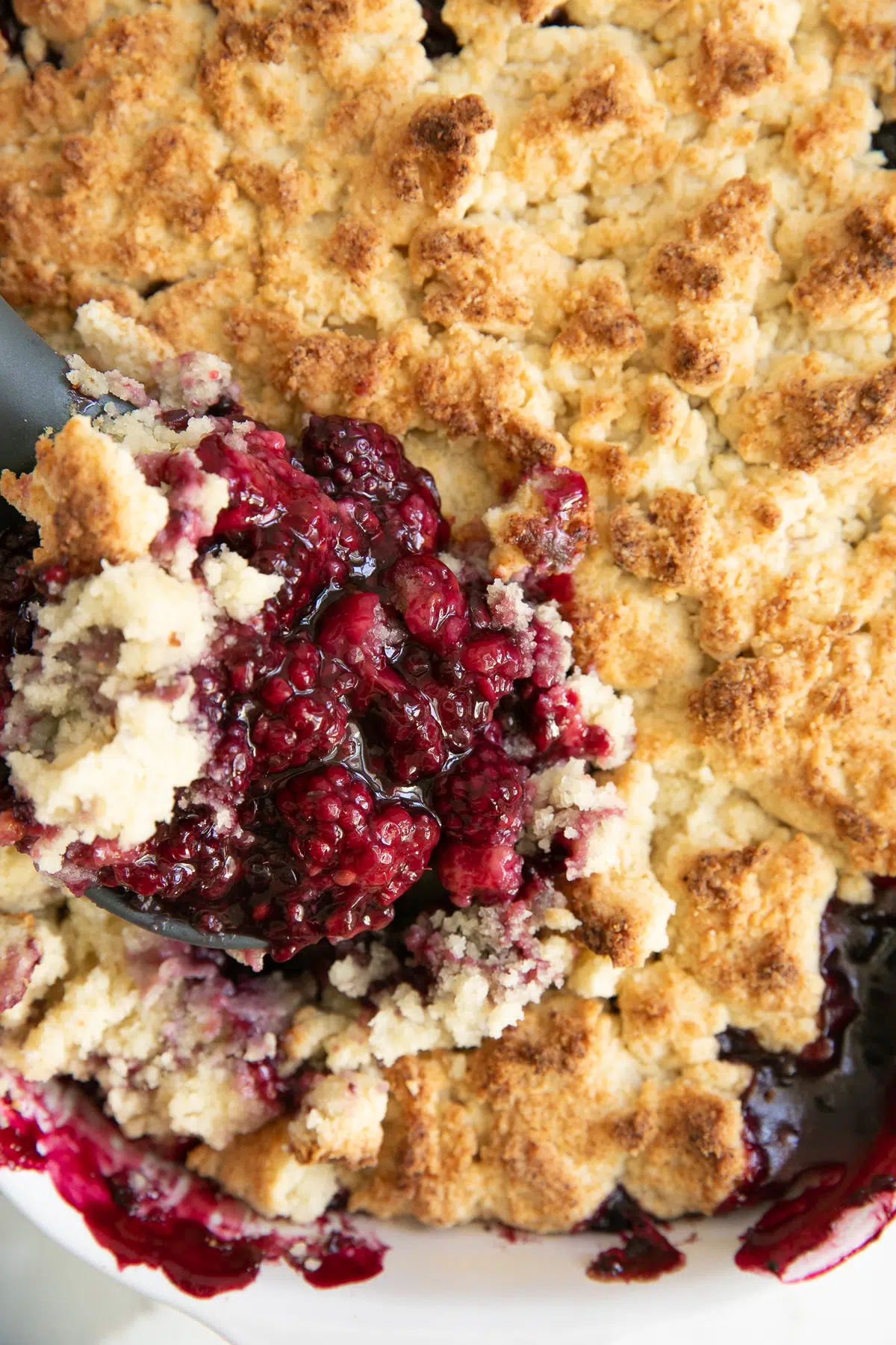 Close up of a rubber spatula digging into a blackberry cobbler.