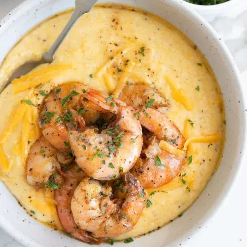 White bowl filled with cheese grits topped with cooked shrimp and garnished with fresh parsley.