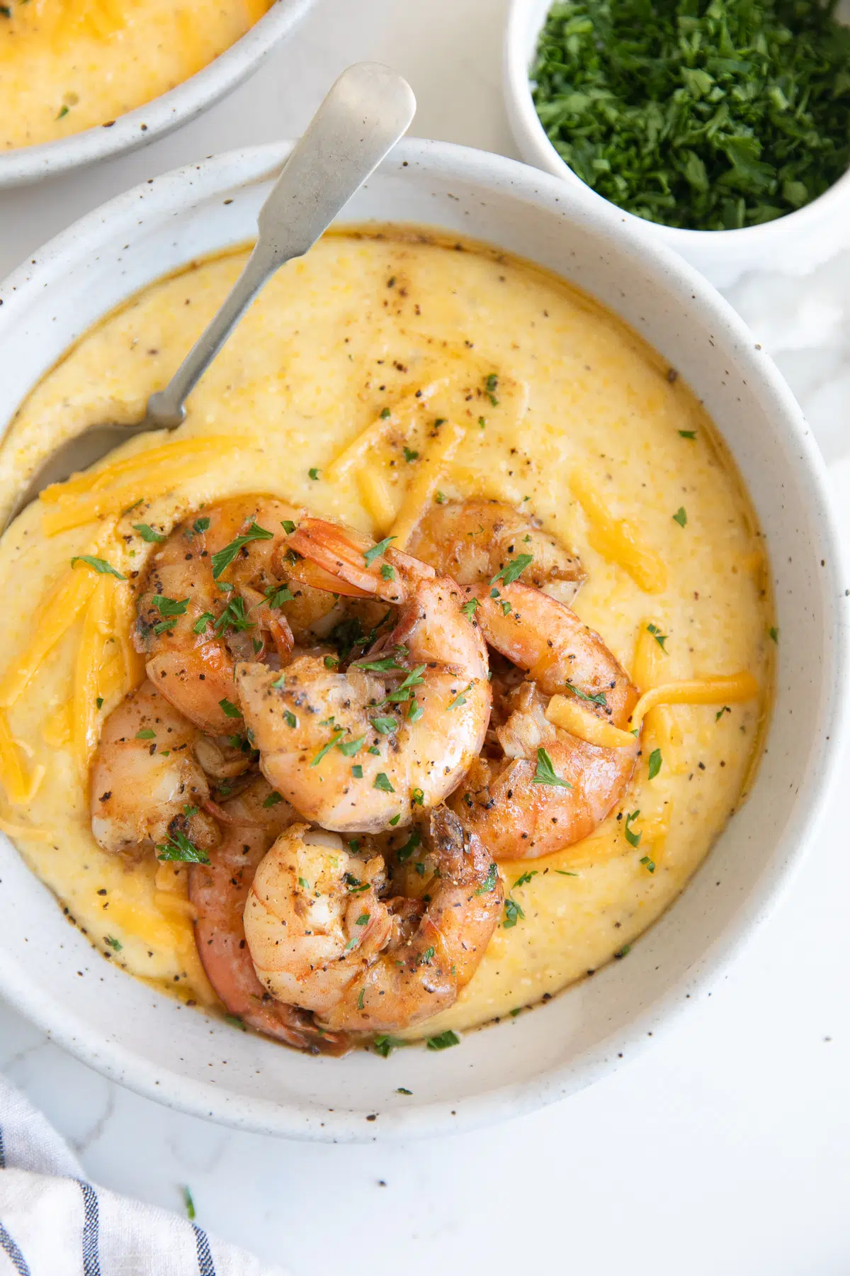 White bowl filled with cheese grits topped with cooked shrimp and garnished with fresh parsley.