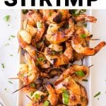 Grilled shrimp wrapped in crispy bacon, served on a white platter and garnished with fresh chopped parsley.