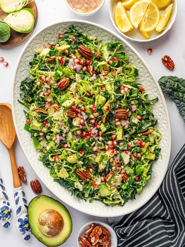 Finished Brussels sprout salad on an oval platter with lemon wedges and avocado