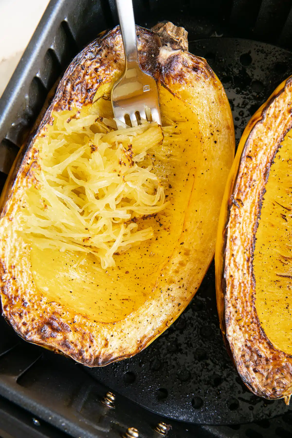 One whole cooked spaghetti squash cut in the air fryer basket cut side up.