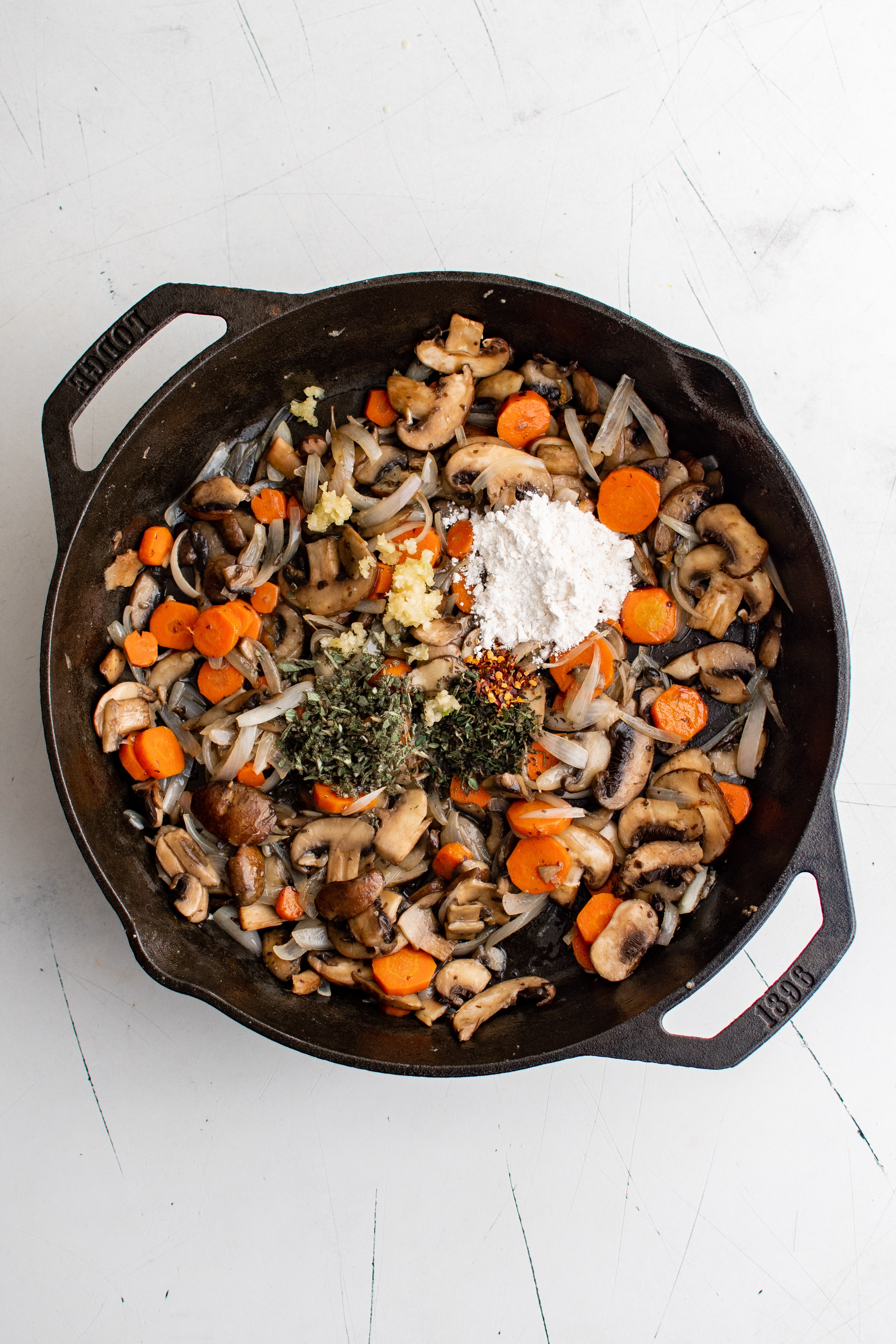 Fresh thyme, fresh sage, and all purpose flour added to a cast iron pan filled with softened carrots, onion, and mushrooms.