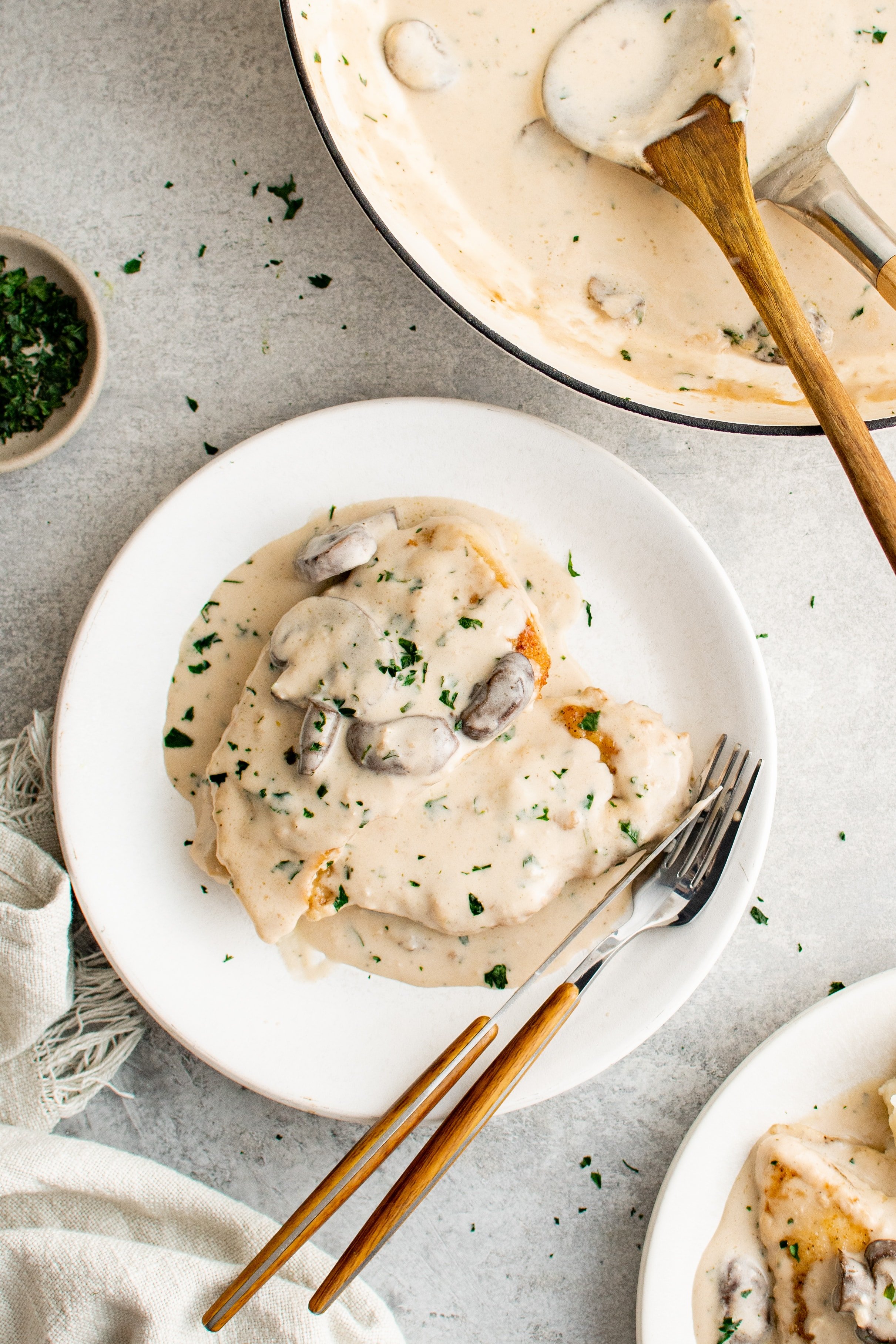 White dinner plate with a scoop of mashed potatoes topped with a piece of chicken and smothered in marsala cream sauce filled with mushrooms.