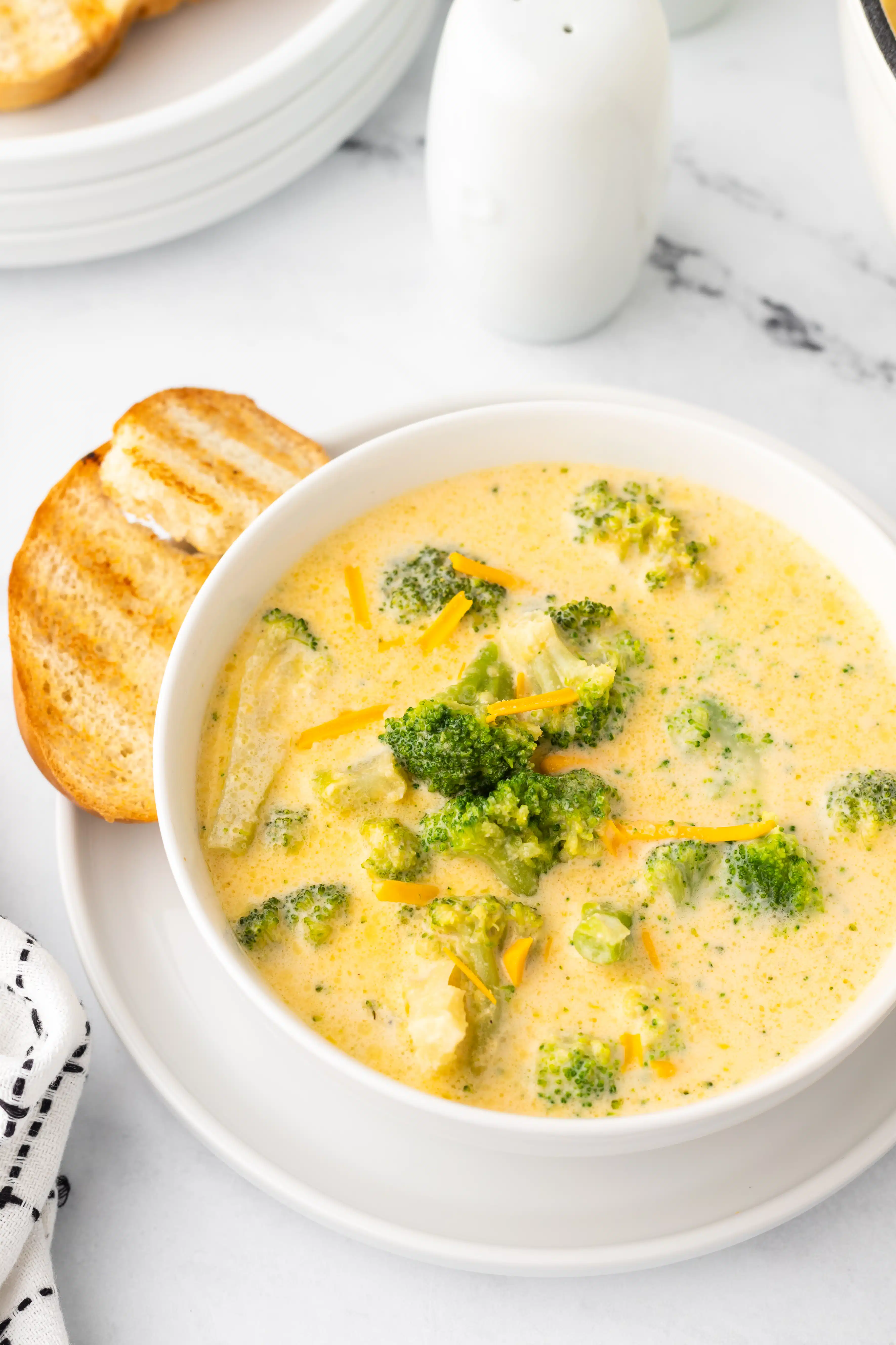 White soup bowl filled with broccoli cheddar soup and served with toasted bread on the side.