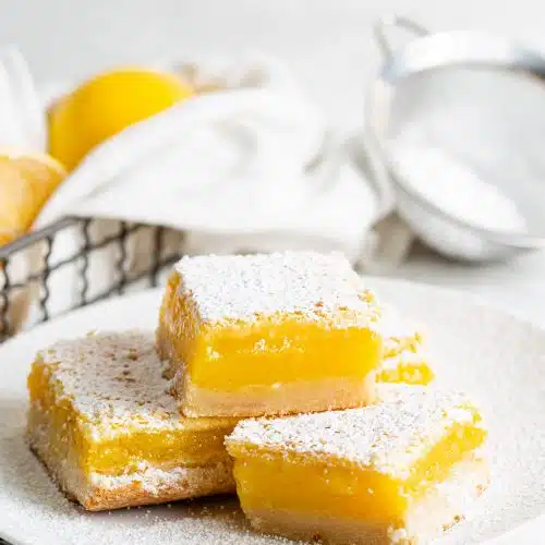 Several sliced lemon bars dusted with powdered sugar on a white plate.