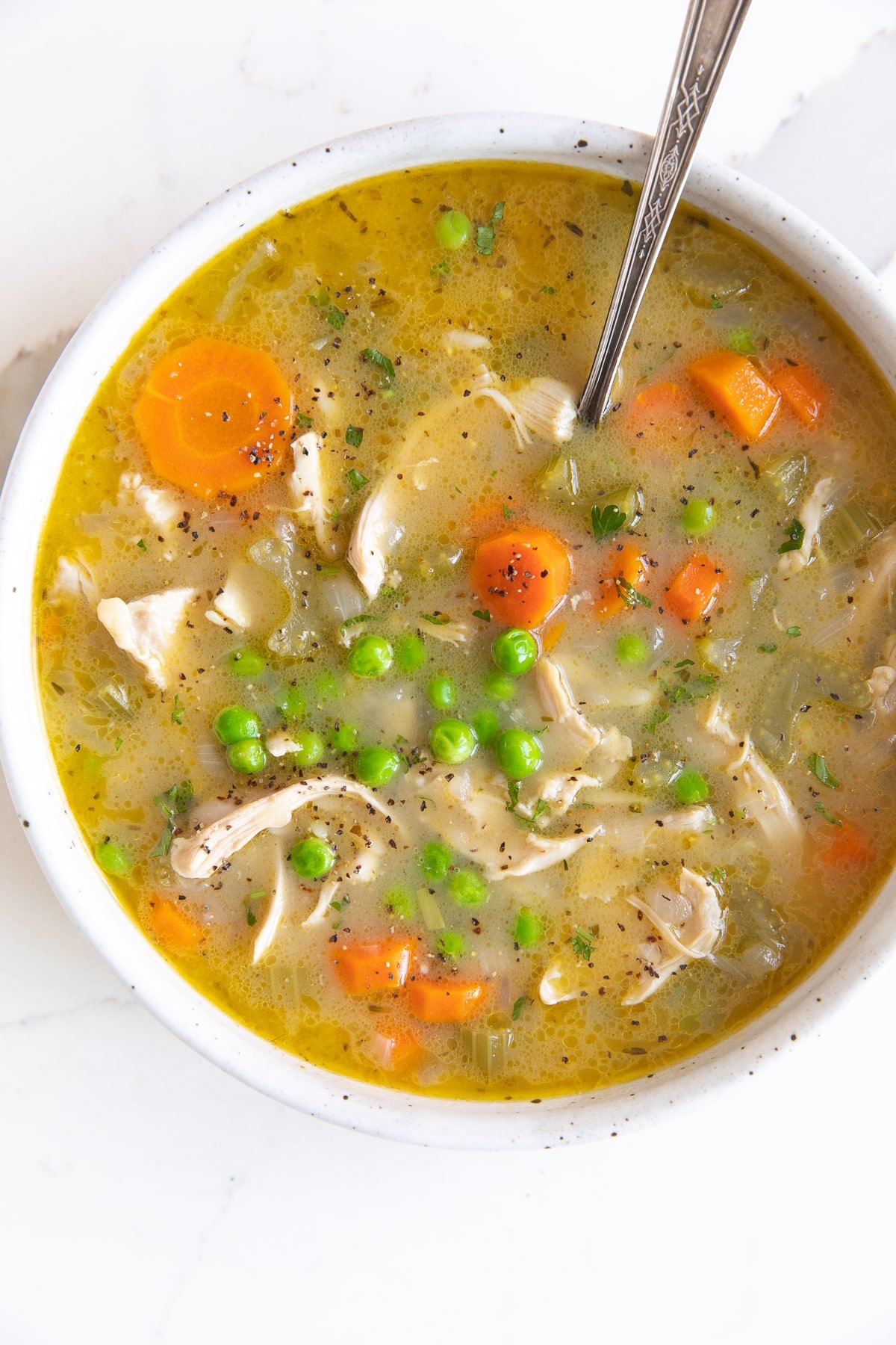 Shallow white soup bowl filled with lemon chicken orzo soup filled with shredded chicken, carrots, celery, orzo, and peas.