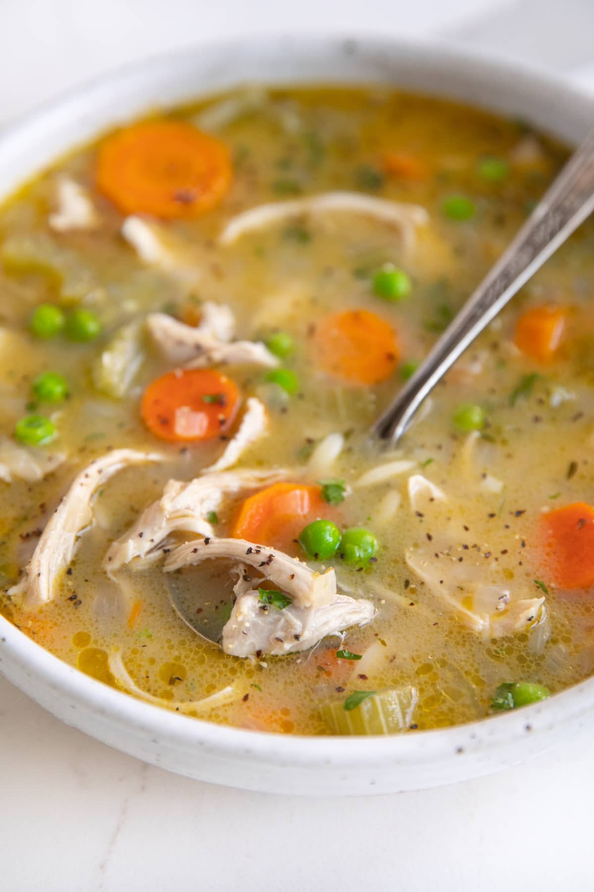 Ciotola di zuppa bianca poco profonda riempita con zuppa di orzo di pollo al limone ripiena di pollo grattugiato, carote, sedano, orzo e piselli.