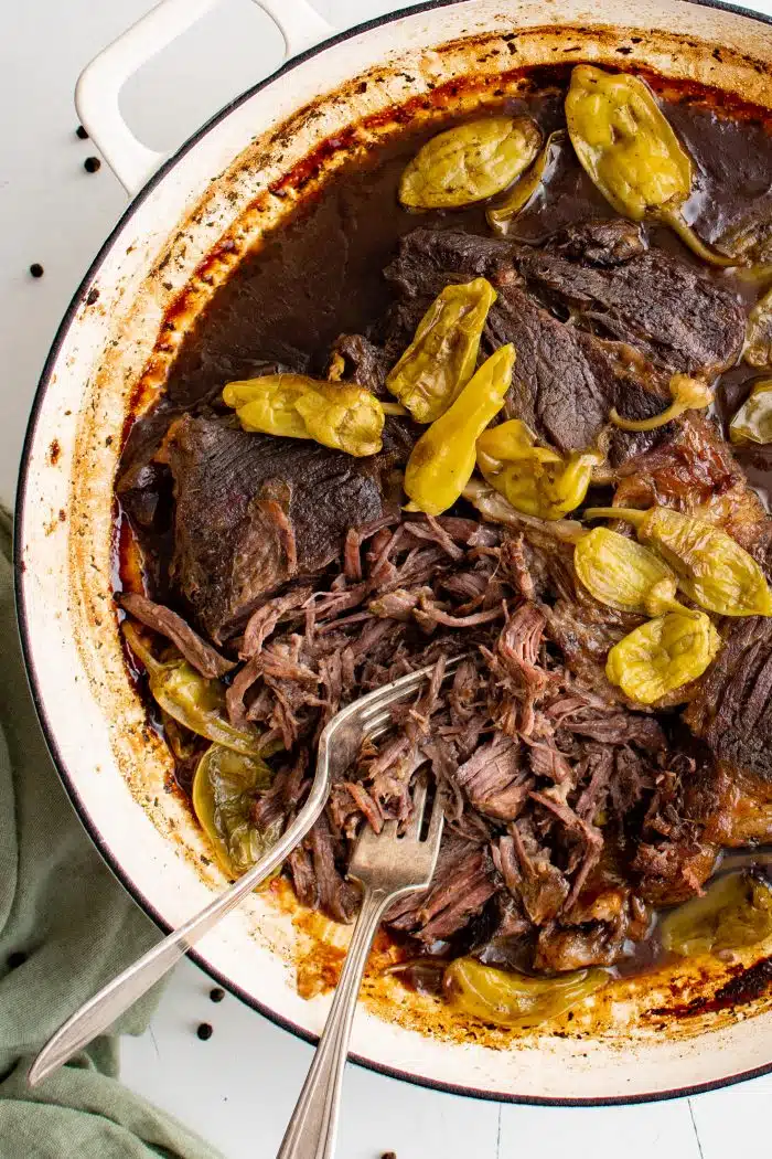 Large enameled Dutch oven filled with Mississippi Pot Roast made with tender shredded beef and pepperoncini.