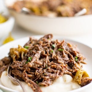 Shredded Mississippi pot roast served over mashed potatoes on a white plate.
