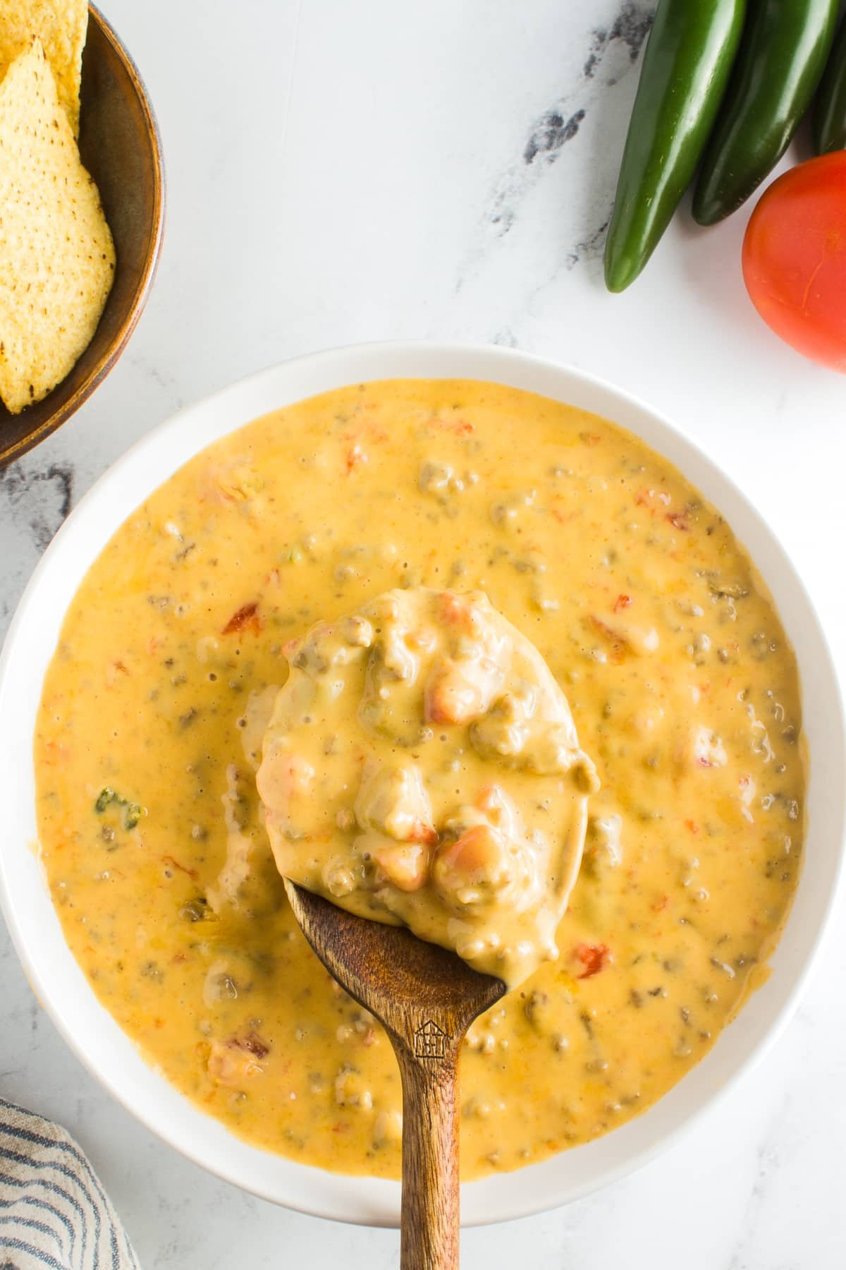 A wooden spoon scooping a serving of hot Rotel Dip from a white bowl, showing the thick cheesy texture with visible tomato and beef chunks.