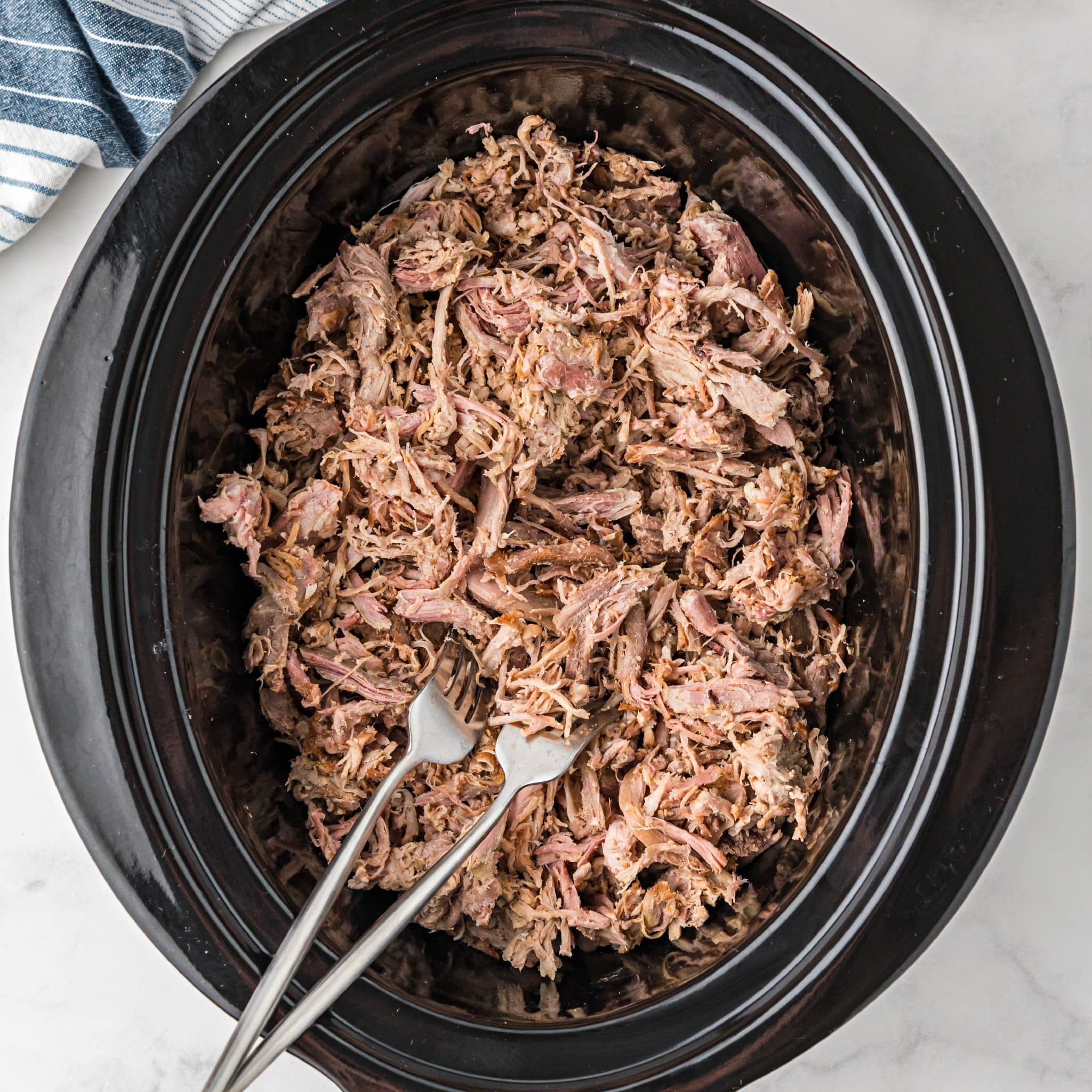 Perfectly tender slow cooker pulled pork shredded and keeping warm in a large slow cooker.