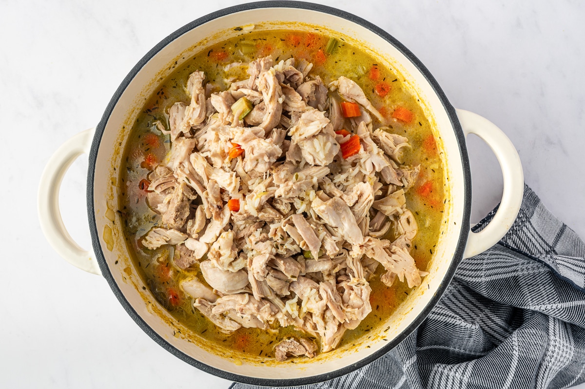 A large amount of shredded chicken added back to a Dutch oven filled with cooked jasmine rice, carrots, celery, and golden chicken broth.