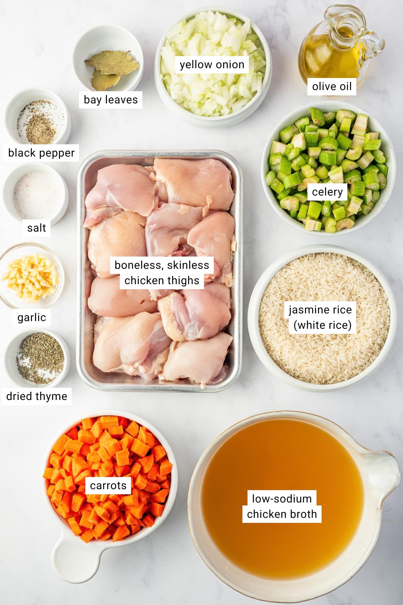 Ingredients for chicken and rice soup arranged in bowls and dishes, including boneless skinless chicken thighs, jasmine rice, low-sodium chicken broth, carrots, celery, yellow onion, garlic, olive oil, dried thyme, bay leaves, salt, and black pepper, with each ingredient labeled.