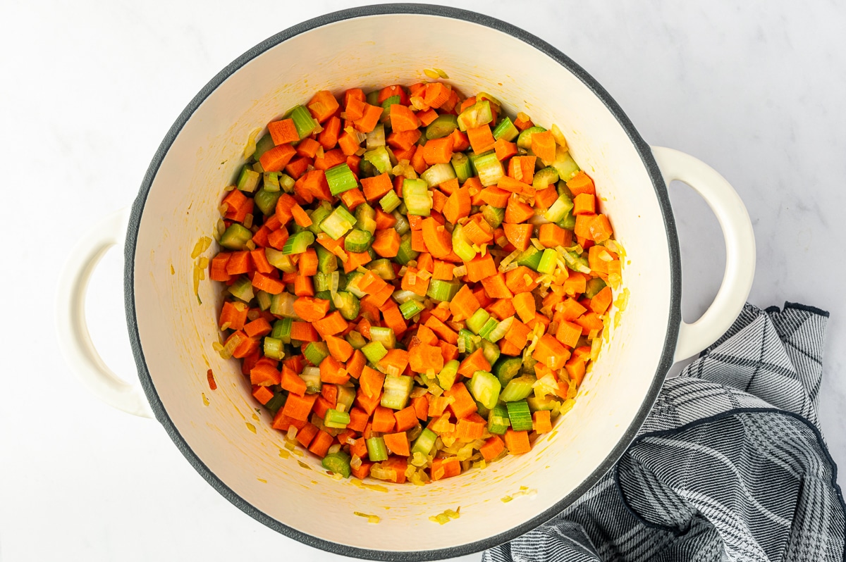 Diced carrots, celery, and onion sauteing in olive oil in a white enameled Dutch oven until beginning to soften.