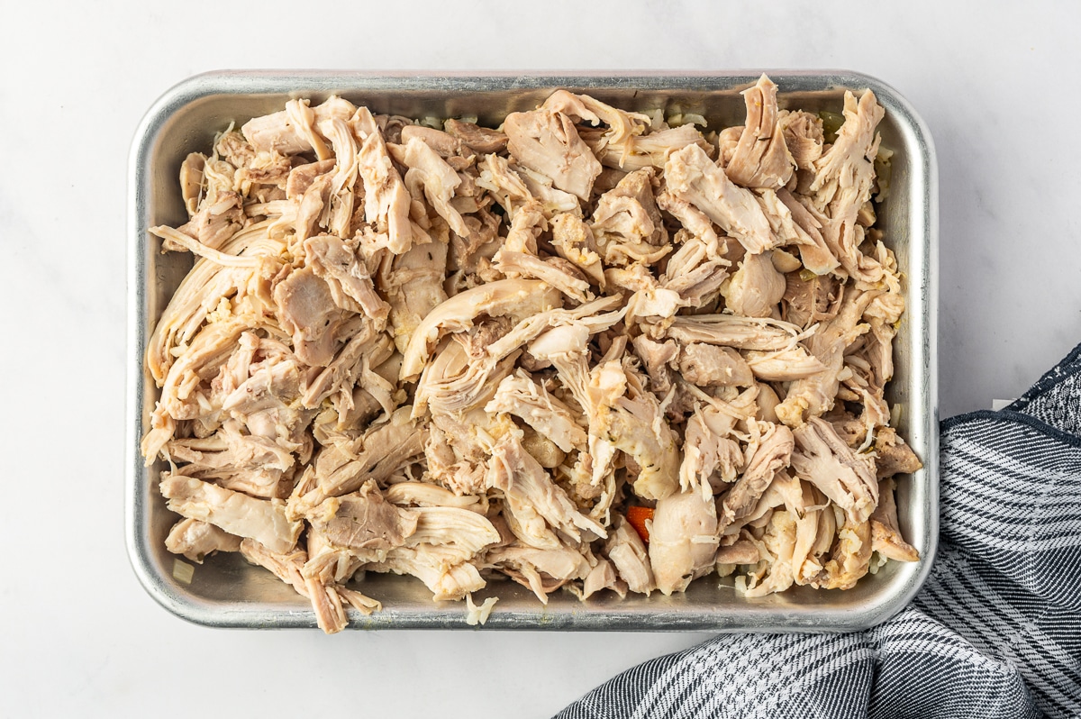 Cooked chicken thighs shredded into bite-size pieces and spread across a small metal tray before being returned to the soup.