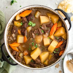 Large pot filled with simmering beef stew made with beef, potatoes, carrots, onions, in a red wine broth and garnished with fresh parsley.