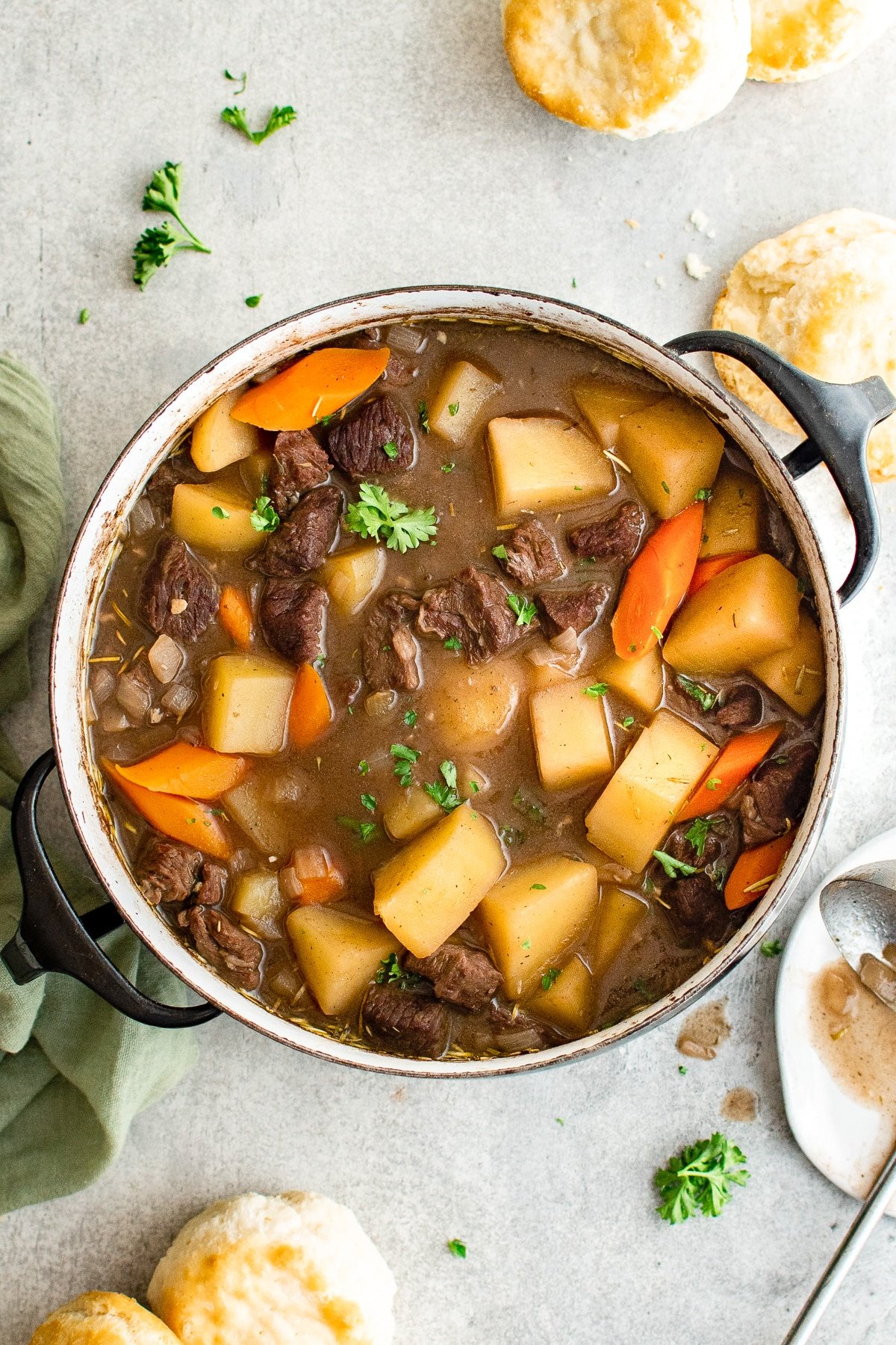 Large pot filled with simmering beef stew made with beef, potatoes, carrots, onions, in a red wine broth and garnished with fresh parsley.