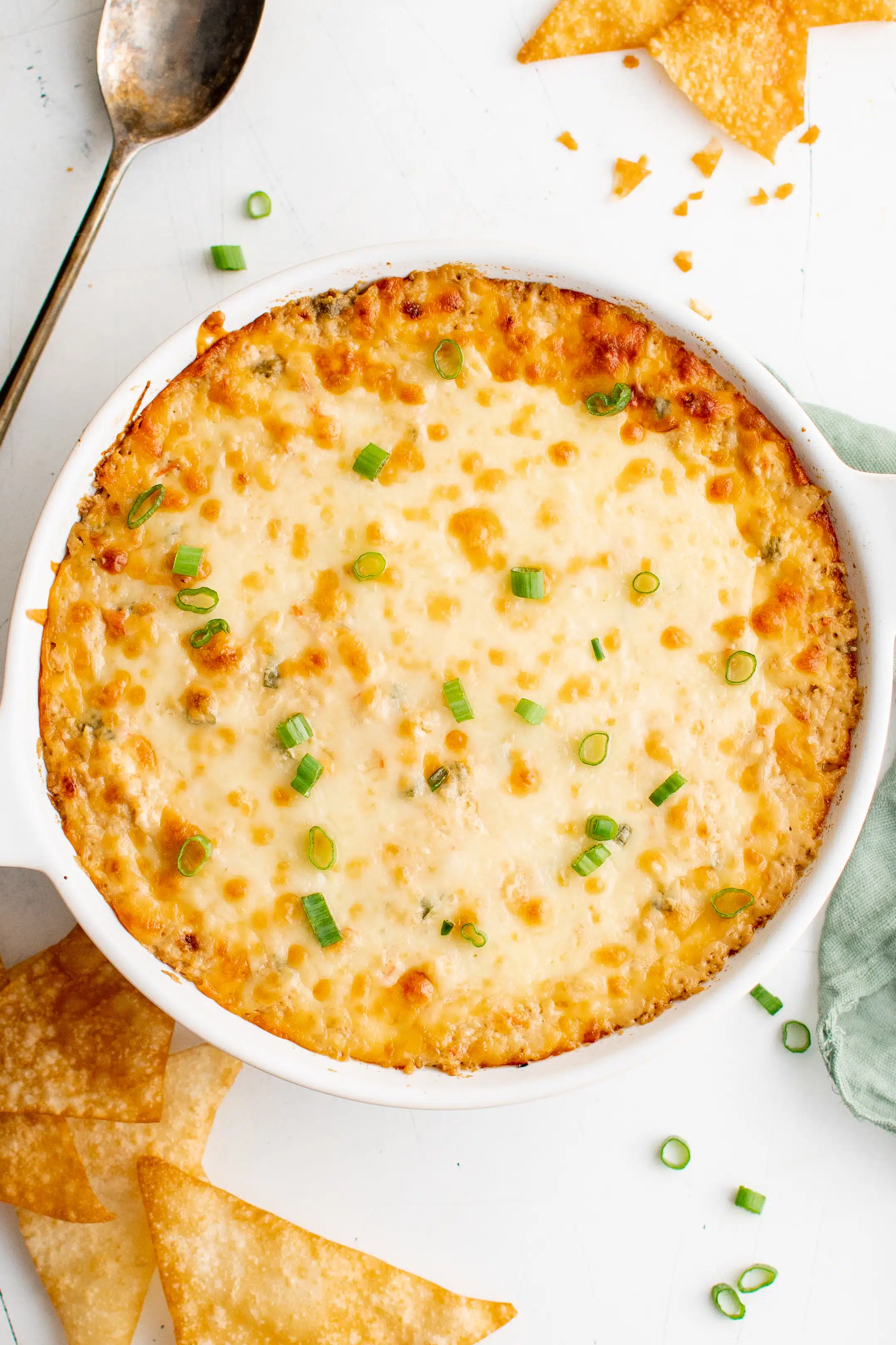 Golden bubbly and cheesy crab rangoon dip in a round white baking dish and garnished with green onions.