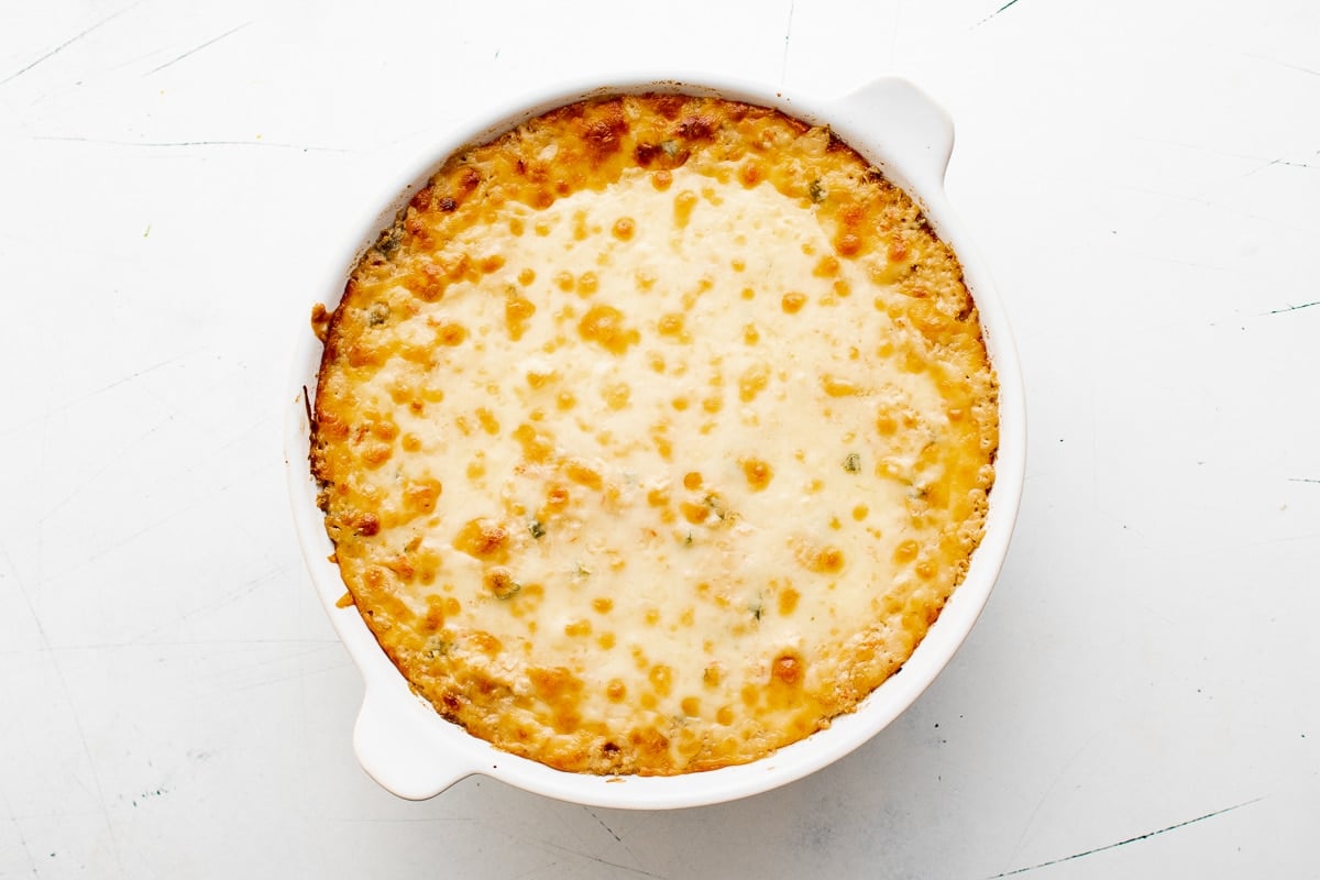 A golden-brown baked crab rangoon dip in a round baking dish, bubbling around the edges.
