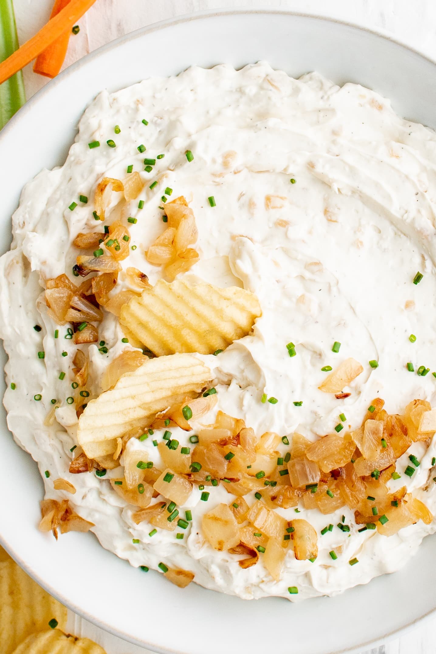 Large round white bowl filled with homemade French onion dip topped with golden caramelized onions and chopped chives.