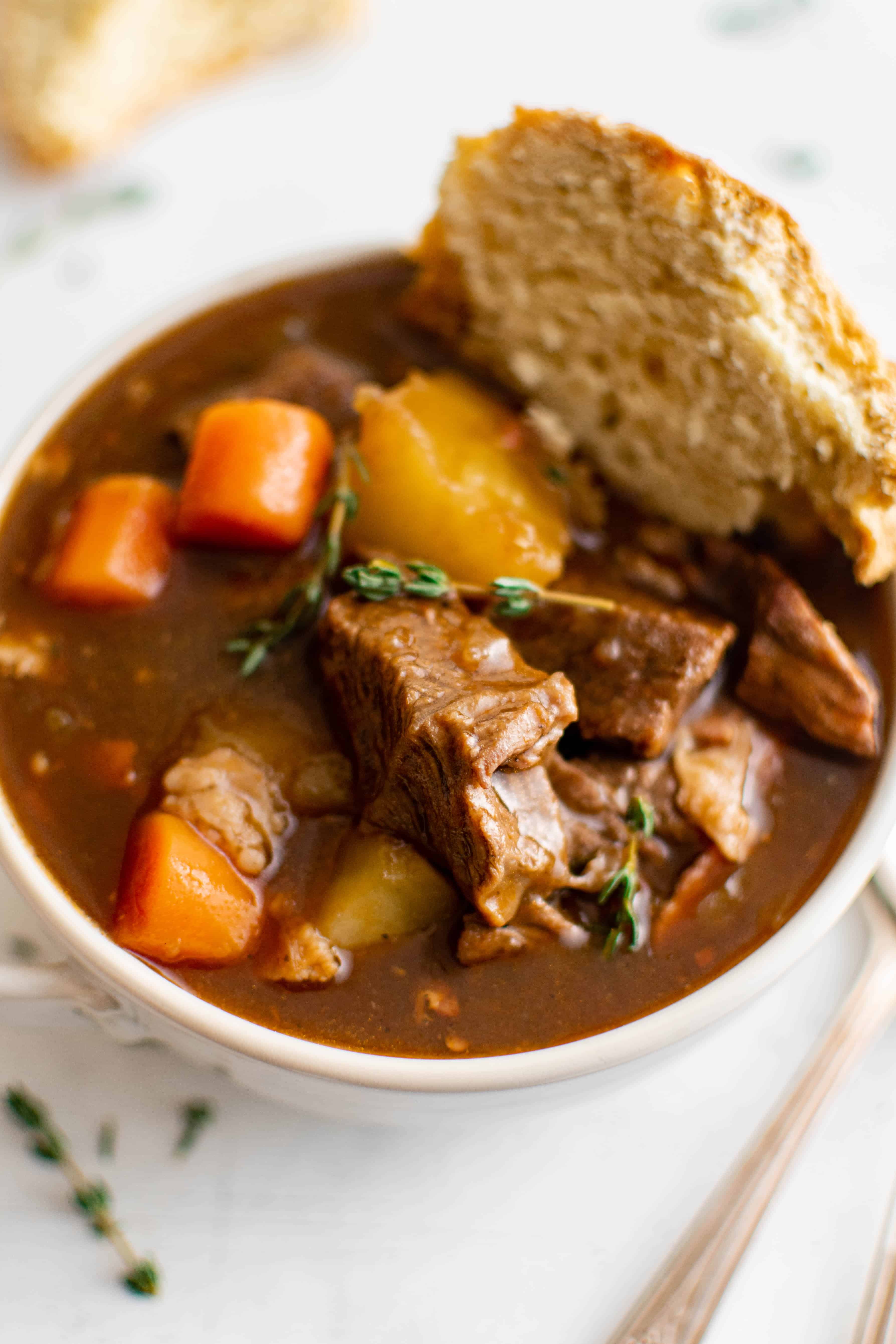 White soup bowl filled with Guinness beef stew filled with chunks of beef, potatoes, carrots, and served with a side of rustic bread.